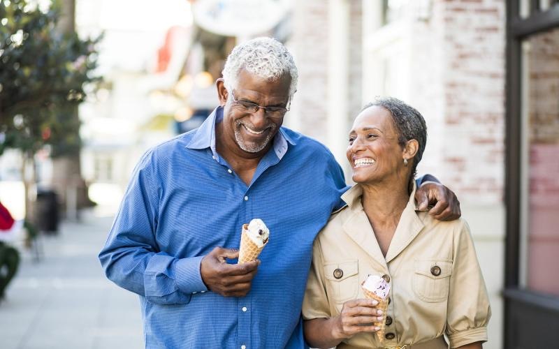 older couple walks down city sidewalk while holding ice cream cones